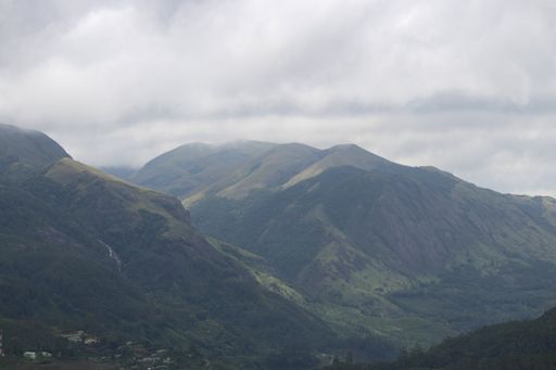 an aerial view of a green mountain covered in plants and trees under the clouds