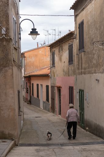 A senior man with a dog walking down a narrow street in the idyllic village of Capoliveri, Island of Elba, Italy