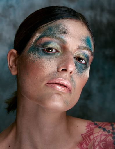 A selective focus shot of an Italian girl with turquoise paint on her face and a shoulder tattoo