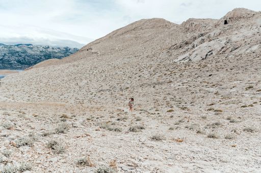Tiny human walking on gravel path on rocky terrain. Hiking, adventure, vast space, mountains. Island Pag, Croatia.