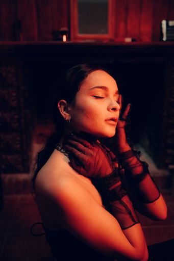 A portrait of a young sexy confident woman wearing fashionable long gloves having her eyes closed in an artificially lit room