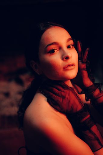 A closeup shot of a young woman's face wearing fashionable long gloves with a confident facial expression in an artificially lit room