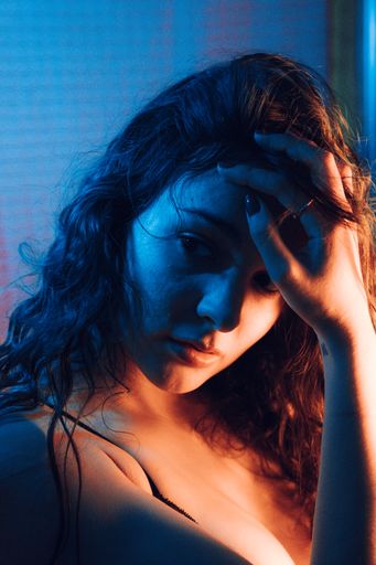 A portrait of a young sexy woman fixing her long hair in an artificially blue-lit studio