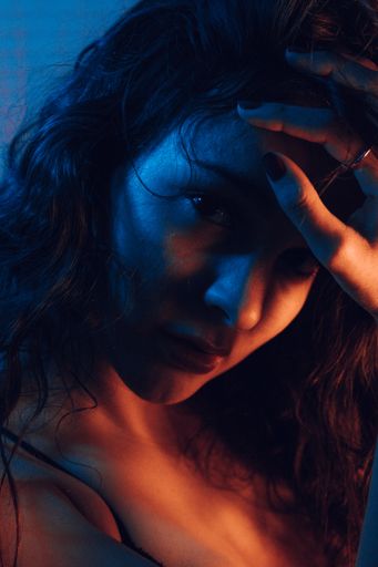 A portrait of a young sexy woman looking at the camera while fixing her long hair in an artificially blue-lit studio