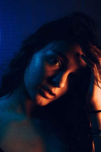 A portrait of a young sexy woman looking at the camera while fixing her long hair in an artificially blue-lit studio