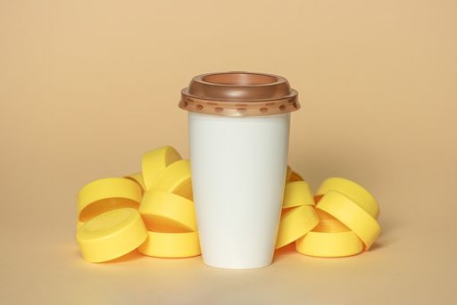 A closeup shot of a coffee cup and a stack of yellow plastic bottle caps