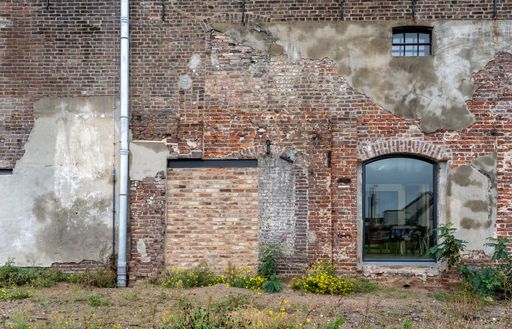 A stunning stot of an old brick wall of a building with a big and small window and steel pole