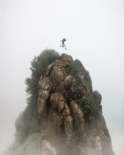 A fantasy concept - a person jumping over a high rocky cliff with a blurred foggy white background