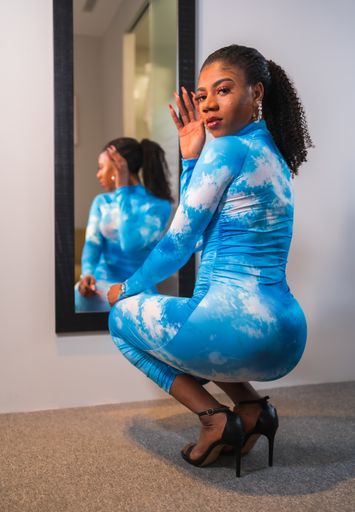 An African American female with collected hair and a blue dress, crouched in front of the mirror