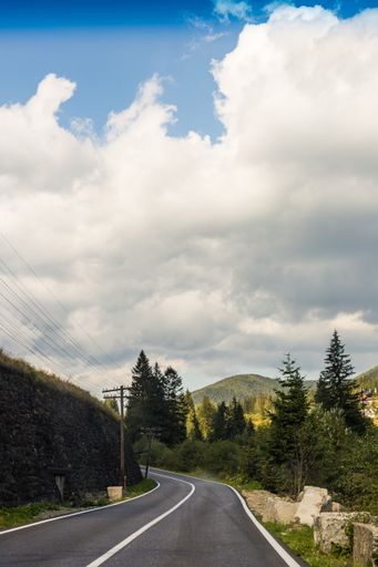 A vertical shot of an empty asphalt road through mountains under a cloudy