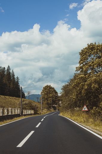 A vertical shot of an empty asphalt road through mountains under a cloudy sky