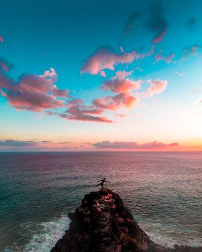 A male standing on rocks near the beautiful sea and amazing breathtaking pink clouds in the blue sky