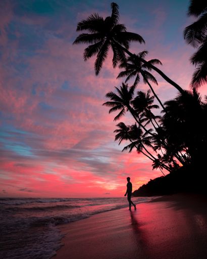 A silhouette of a male on the beach during sunset with amazing clouds in the pink sky