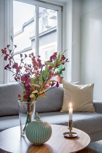 A vertical shot of flowers in a vase and a candle on a table near a couch