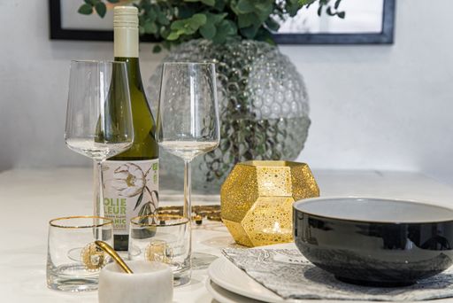 Dinner table with wine and wine glasses, a round vase with green plants candle light a bowl and plate.