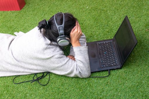 Young Woman Lying on the Grass is Works on her Laptop with Headphones