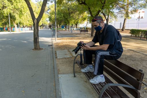 Stock photo of man wearing face mask looking at some photos in his camera while sitting in the park.