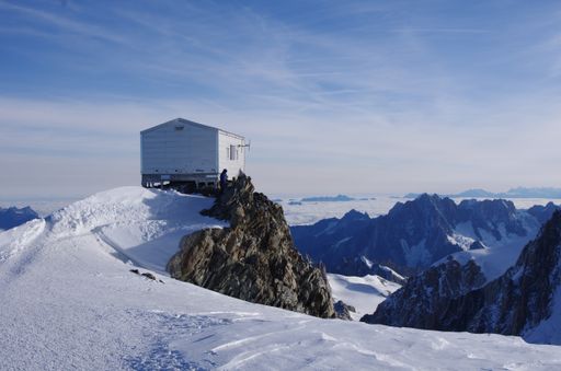 A little wooden hut built on the top of a snowy hill with amazing rocky mountains in the background