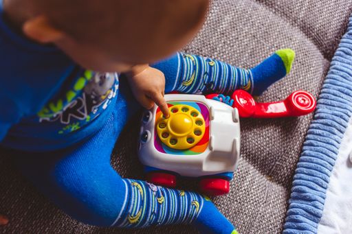 A baby in blue playing with a toy telephone on the couch