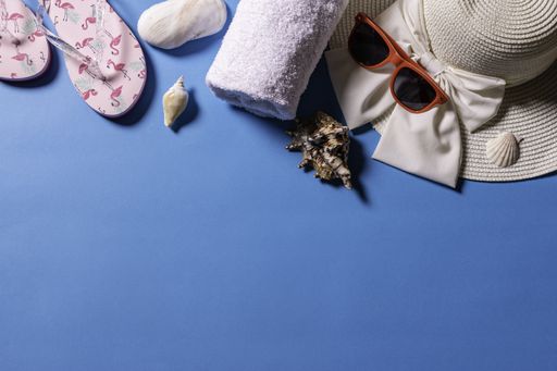 A top view of sunglasses, a straw hat, sandals, a towel and sea shells on a blue background