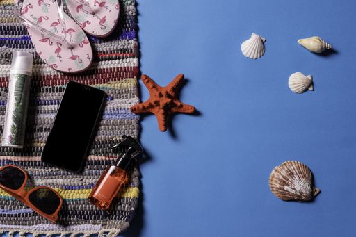 A top view of sunglasses, sandals and sea shells on a blue background