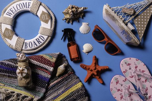 A flat lay shot of sunglasses, sandals and sea shells on a blue background