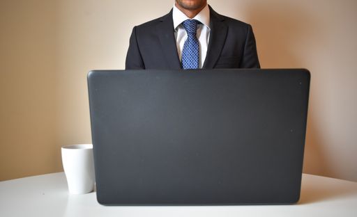 A young man in a suit working on a laptop while drinking coffee