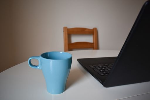 A blue mug and a laptop on a table with a wooden chair in a room