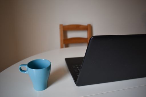 A blue mug and a laptop on a table with a wooden chair in a room