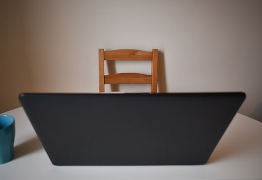 An open laptop and a mug on a desk with a wooden chair in front of it