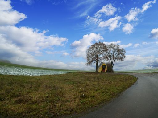 A scenic view of a country road near a field in Bavaria, Germany under a cloudy sky background