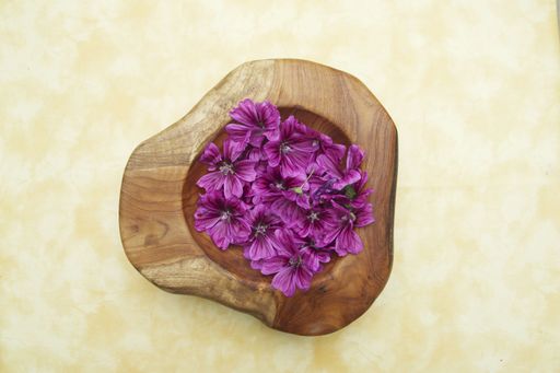 A top view of mallow blossoms in a wooden bowl used for healthcare