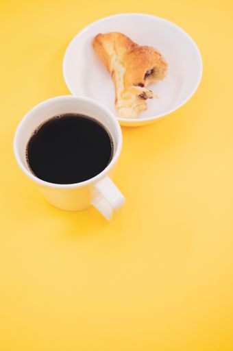 A vertical shot of a cup of coffee and bitten croissant on a white plate isolated on yellow background
