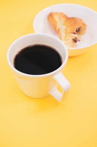 A vertical shot of a cup of coffee and bitten croissant on a white plate isolated on yellow background