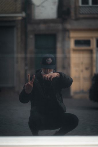 A vertical shot of a male in a cap and face mask doing a mirror selfie in the street in Porto, Portugal - victory sign