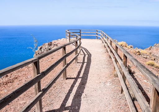 A beautiful shot of a pathway at the top of the cliff with a blue ocean in the background