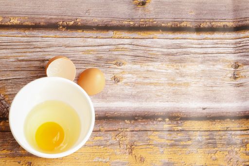 A top view of fresh egg yolk and white in a bowl with eggshells on a wooden rustic table