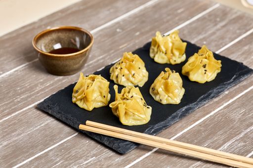 A high angle shot of tasty prawn siu mai on a black plate with chopsticks
