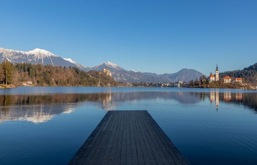 The reflection of the mountains and old buildings in the lake with a wooden pier in the foreground