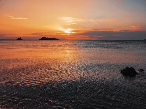 A beautiful view of the sun peeking from above of a mountain during the sunset at the beach