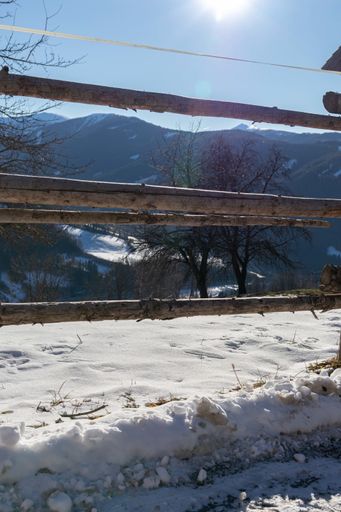 A vertical shot of a wooden fence on a snowy day with mountains  and trees in the background