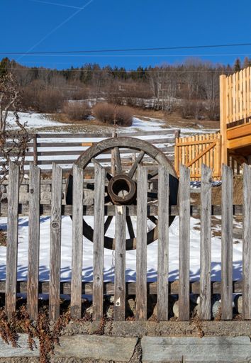 A vertical shot of a wooden wheel behind the fence in the park covered in snow