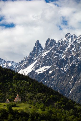 A high angle shot of a church in the Mestia highland in Georgia with the snowy mountains in the background