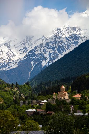 A high angle shot of a church in the Mestia highland in Georgia with the snowy mountains in the background