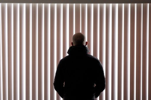 A man standing in front of window shades from behind