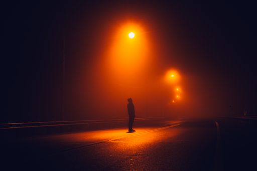 An amazing shot of an unrecognizable man standing in the middle of a highway with red lights at night