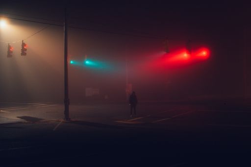 An unrecognizable man standing in the middle of a highway with red lights at night