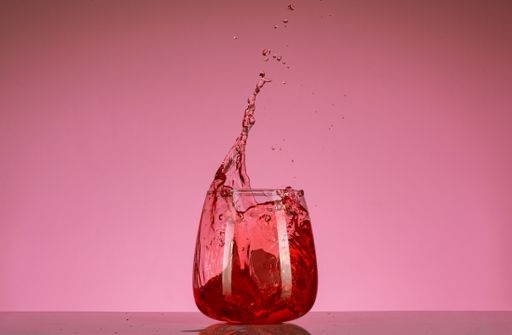 A glass of a red splashing alcoholic drink on a pink background