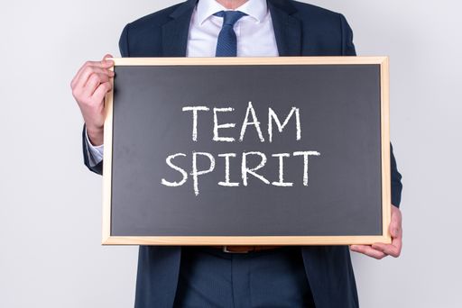 A businessman wearing a suit and holding a blackboard with the phrase Team Spirit written on it