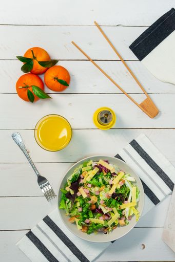 A plate of fresh Mediterranean salad with olive oil served with orange juice on a white wooden table